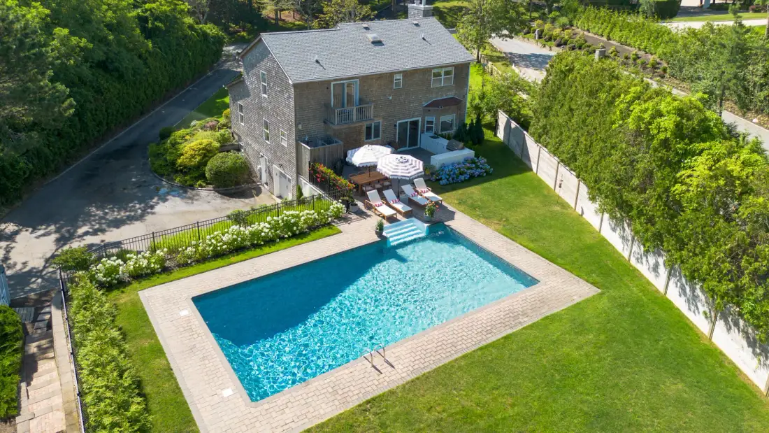 Una piscina en el patio está junto a un césped y una casa de dos pisos.