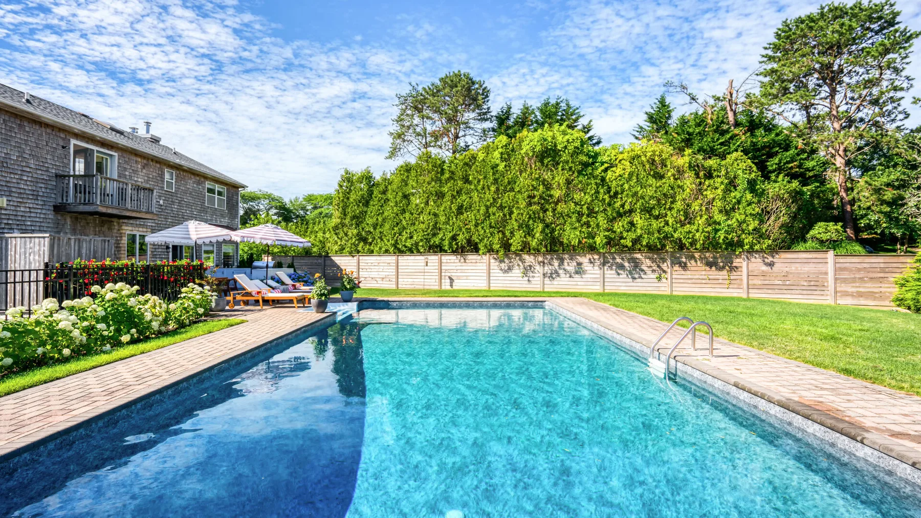 Piscina al aire libre junto a un jardín y una casa.