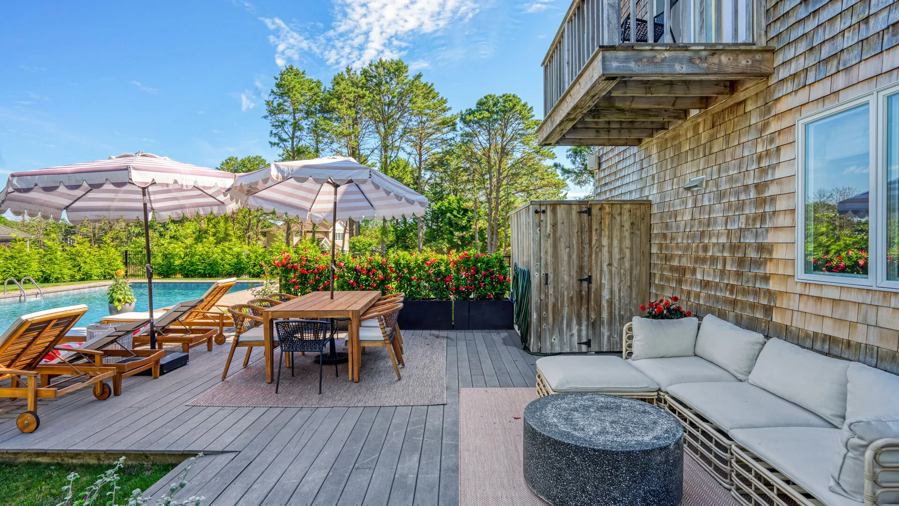 Un patio exterior con piscina, asientos, sombrillas y una mesa junto a una casa revestida de tejas.