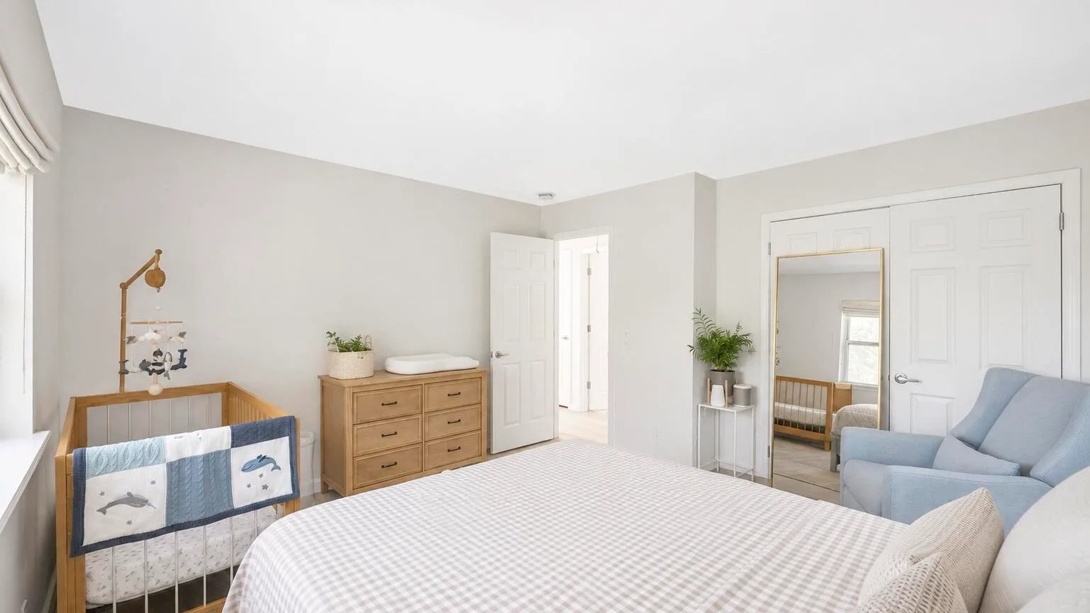 Un dormitorio luminoso con una cuna, una cómoda y asientos.