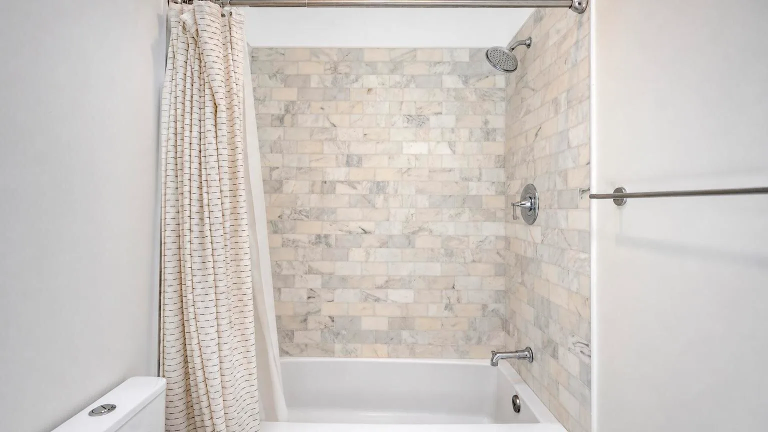 Una ducha y bañera con azulejos están parcialmente cubiertas por una cortina.