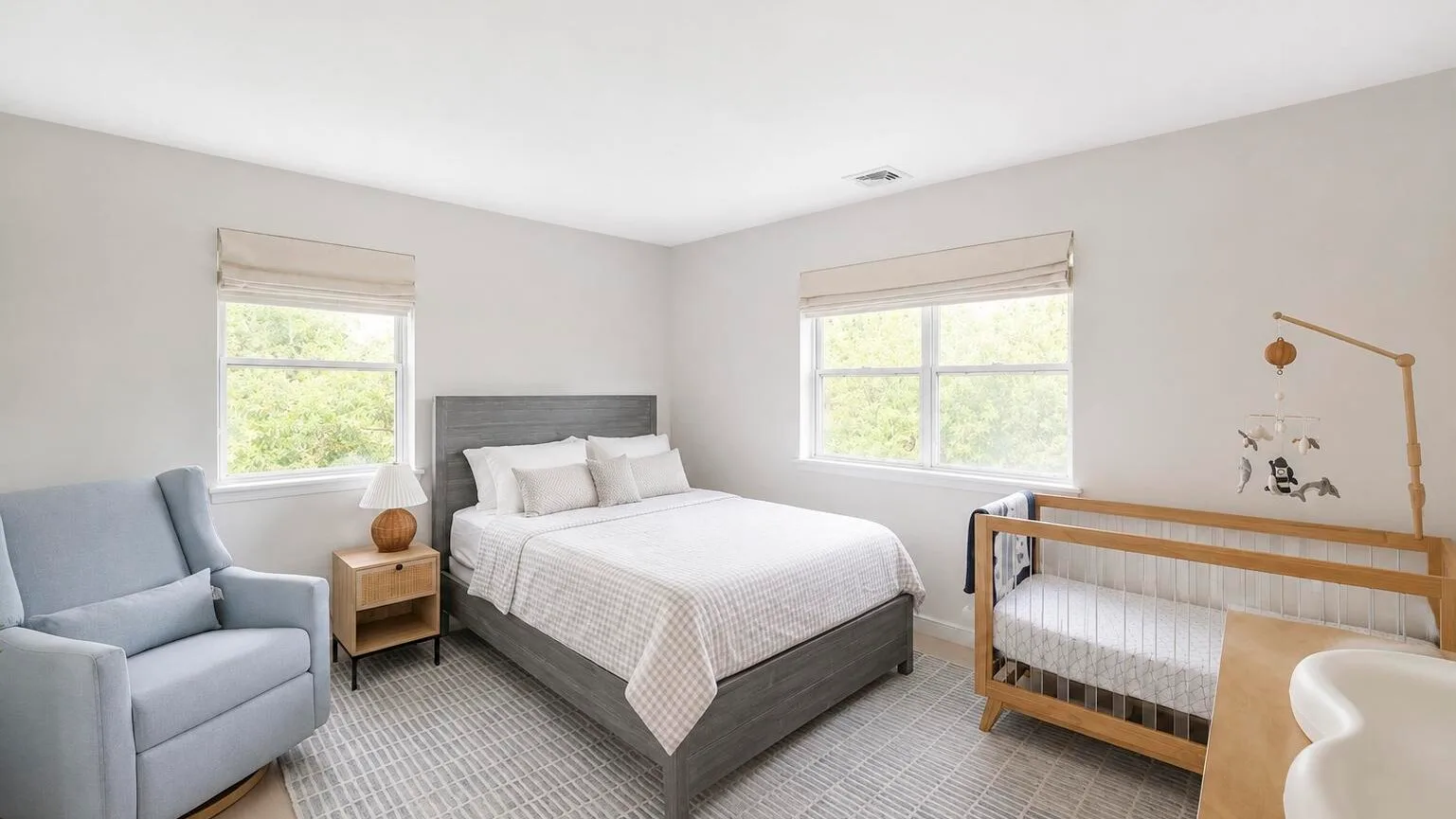 Un dormitorio con una cama, una cuna y una zona de estar junto a las ventanas.