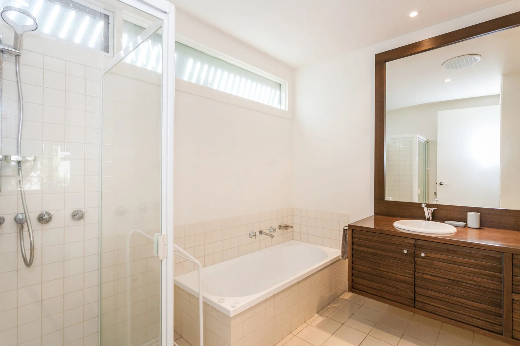 A bright bathroom with a bathtub, glass shower, and wood vanity.