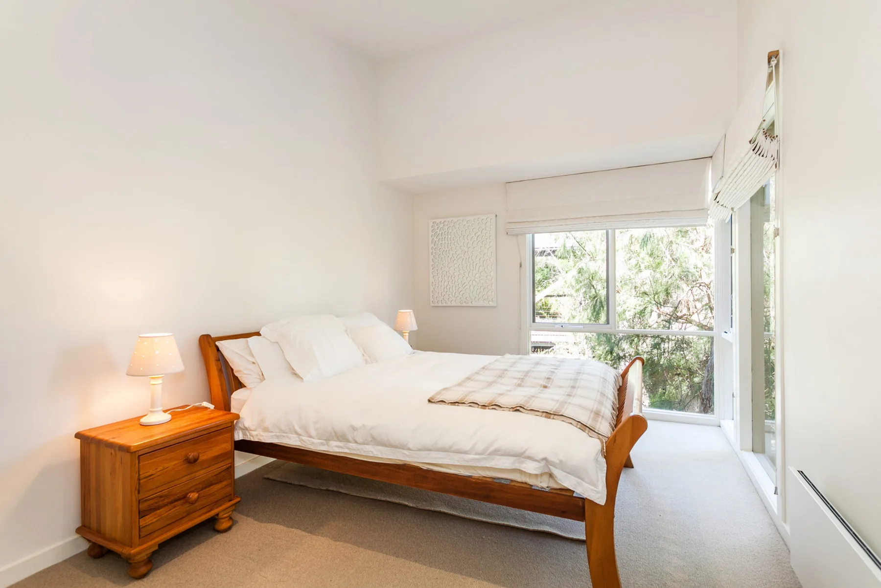 A bright bedroom with a wooden bed and large windows.