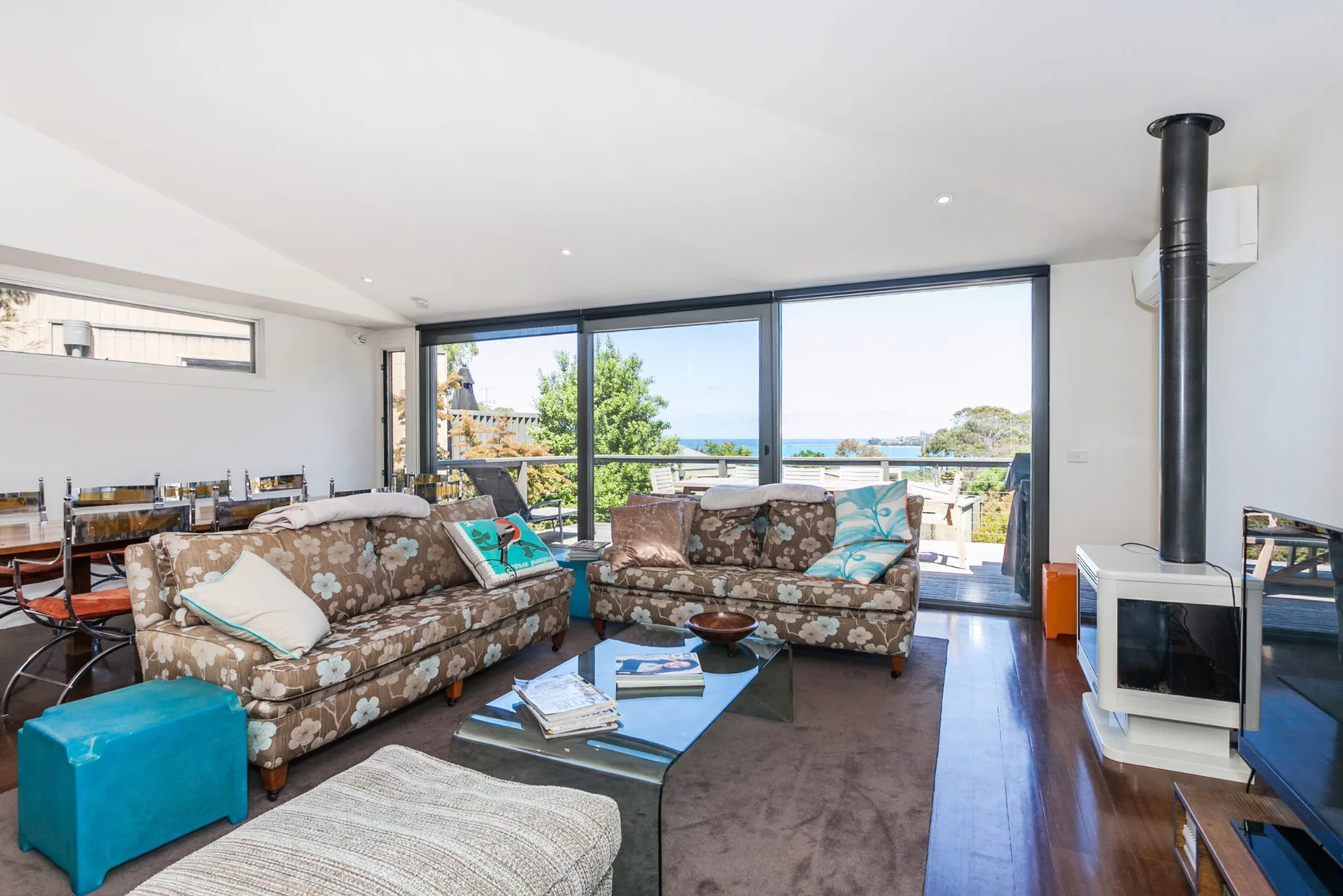 A bright living room with seating arranged beside broad windows overlooking the water.