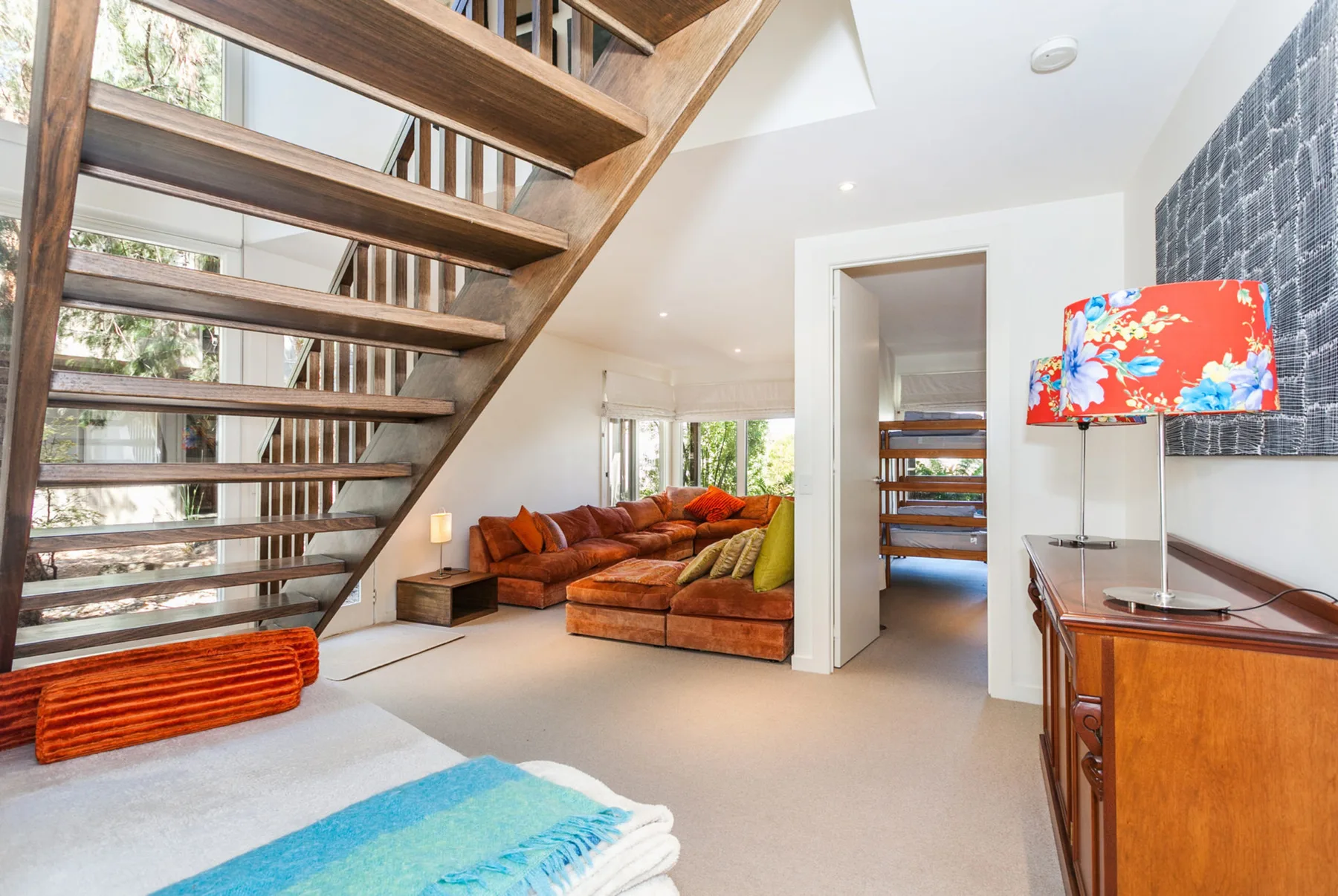 A bright living room with a wooden staircase and sectional seating.