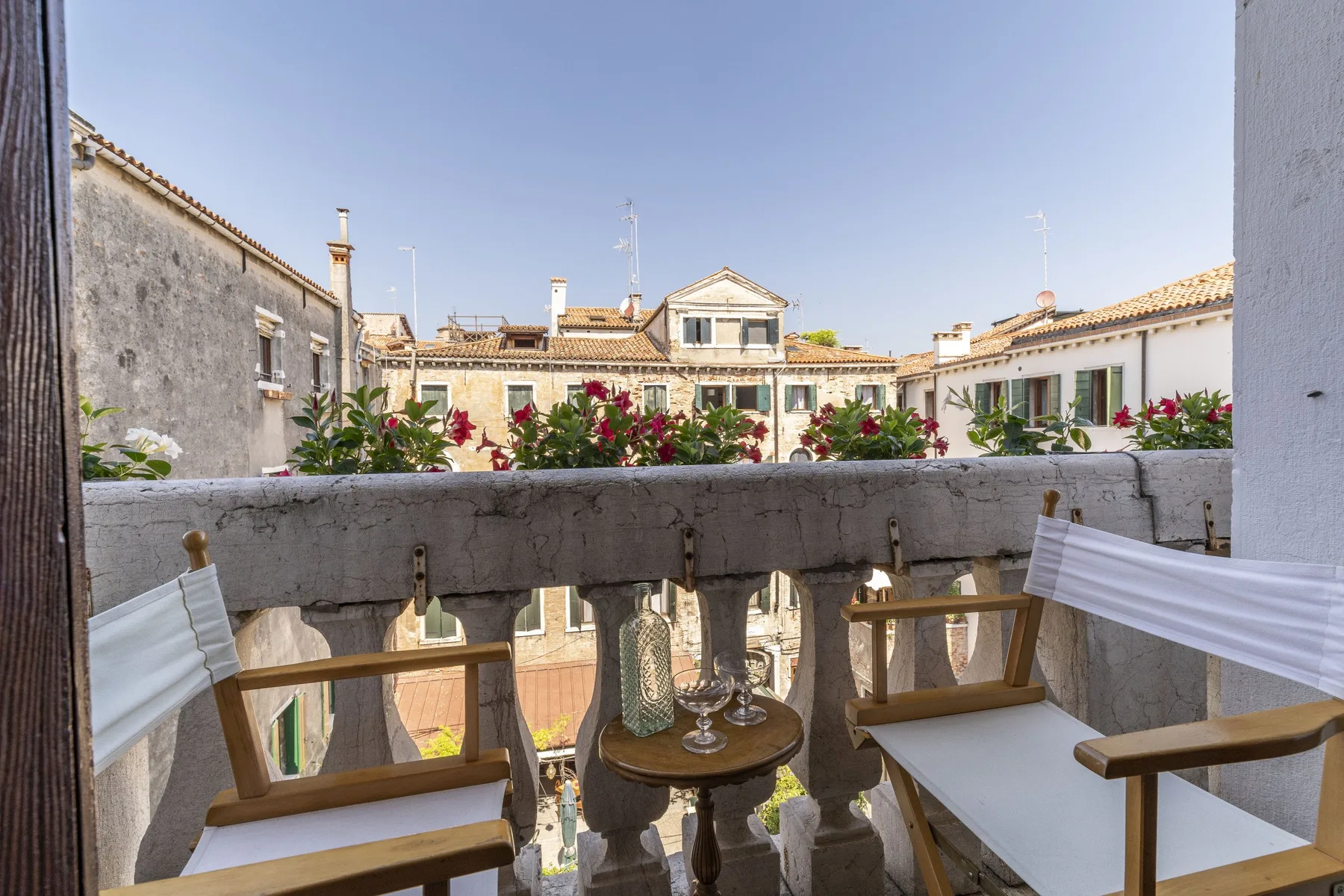 A small balcony seating area overlooks nearby buildings and flowering plants.
