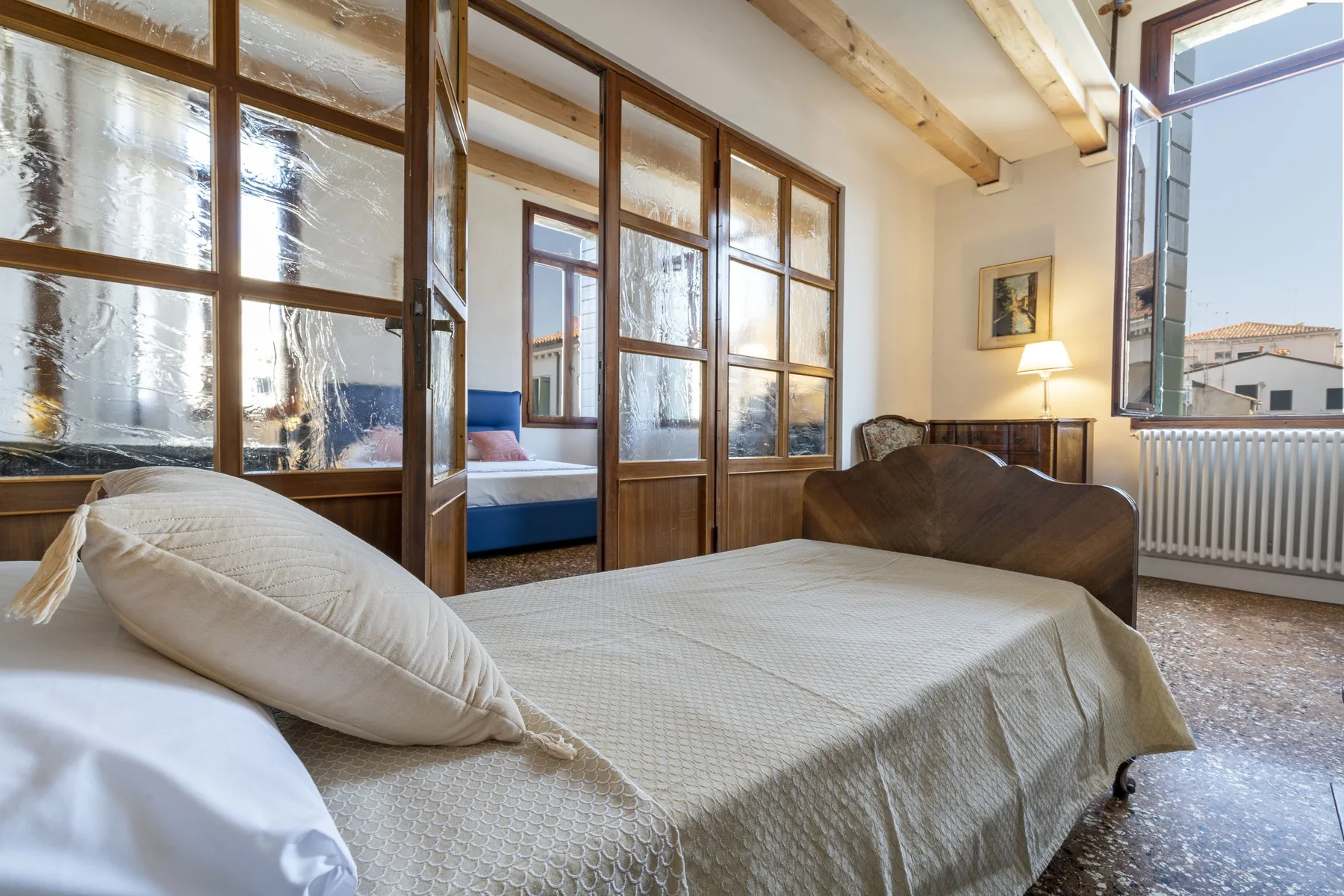 A bedroom with a large bed beside wooden-framed glass partitions and a window.