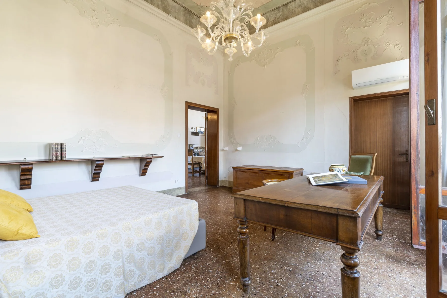 A bedroom with a bed, wooden desk, and chandelier.