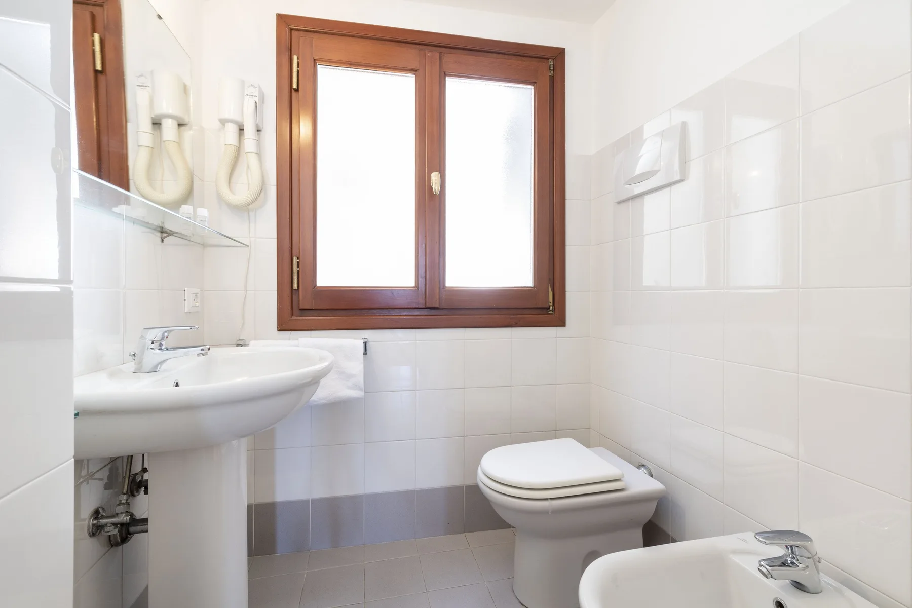 A tiled bathroom with a sink, toilet, and wooden-framed window.