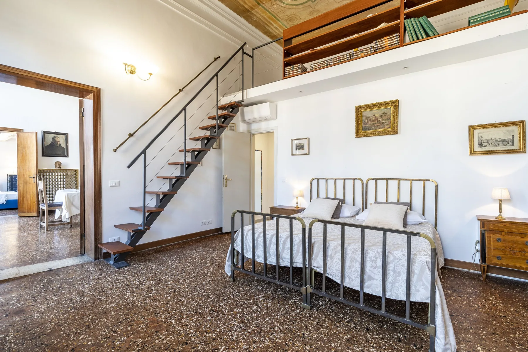 A bedroom with a metal bed and an open staircase leading to a loft.
