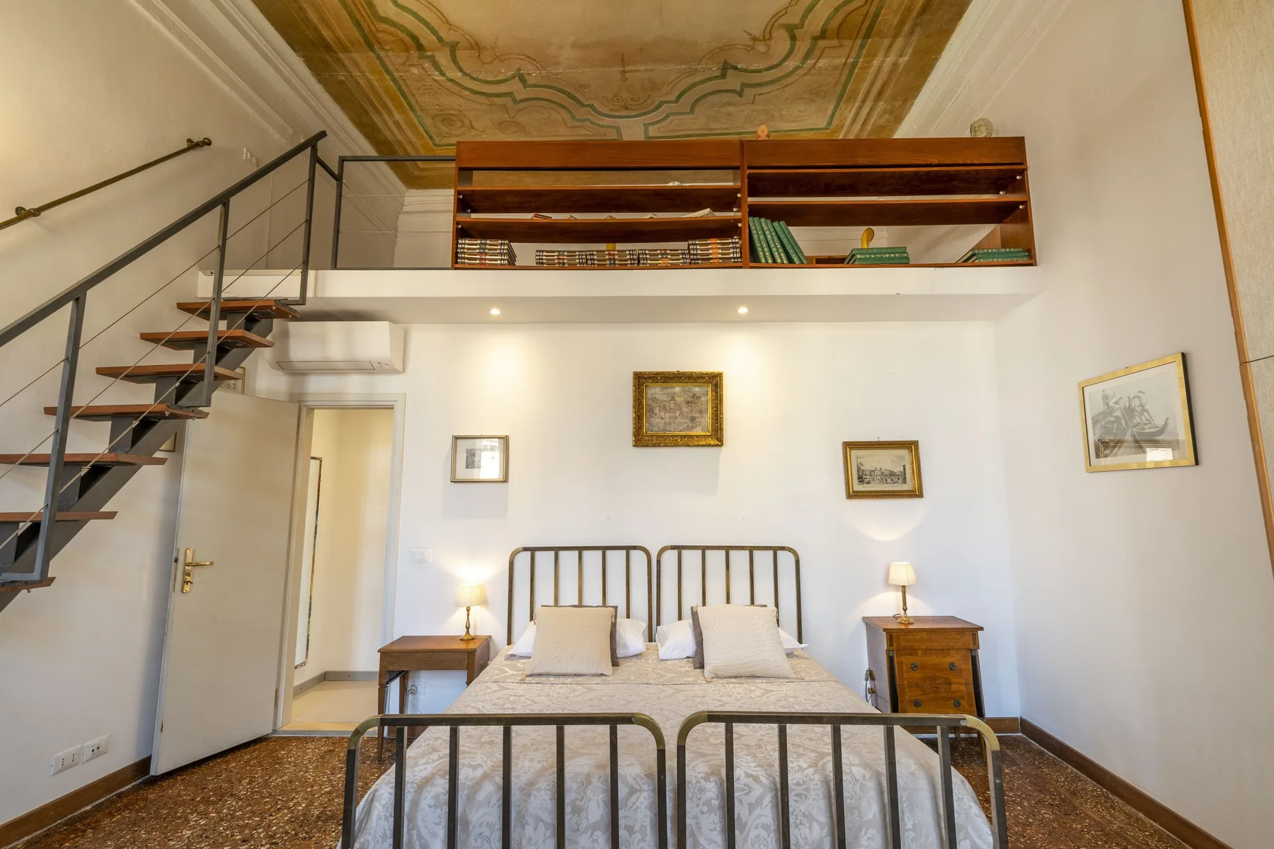 A bedroom with a double bed beneath a mezzanine and an open staircase.