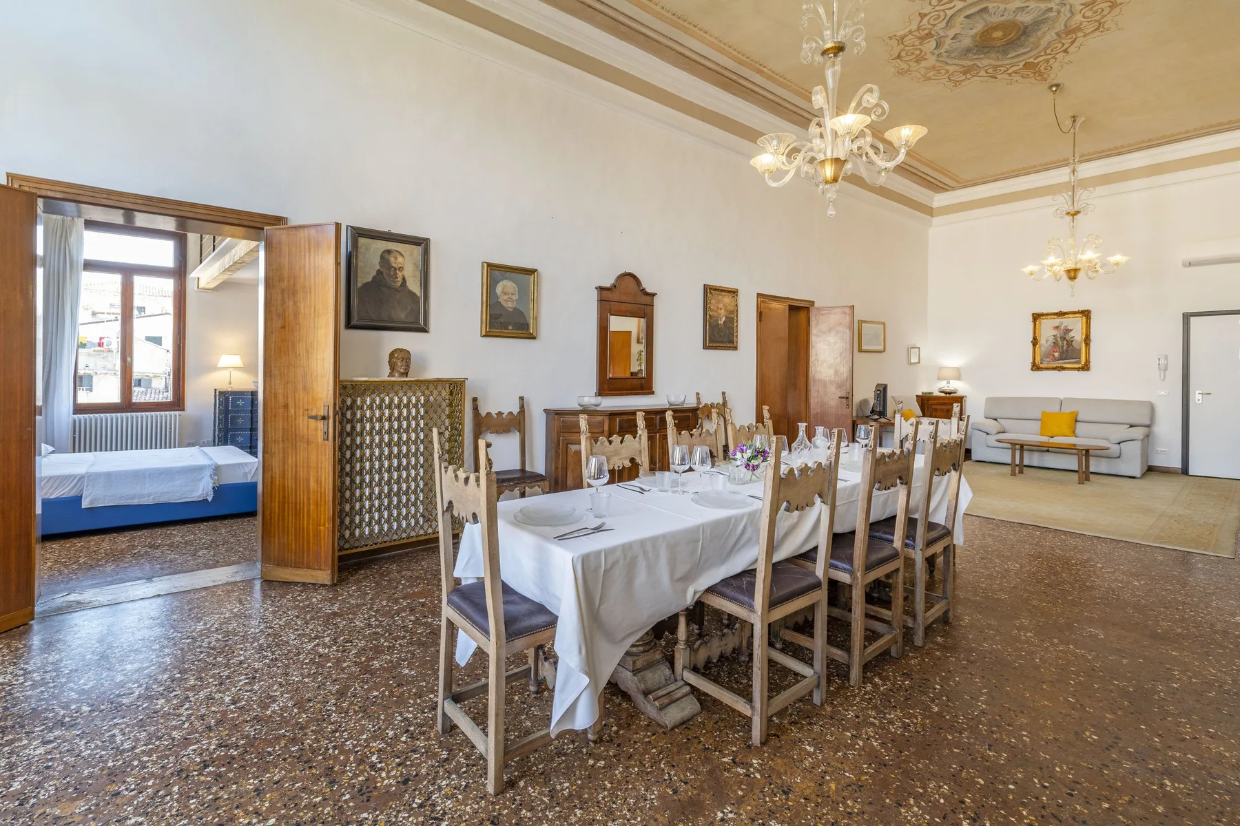 A formal dining room with a long table set with white linens and chairs.