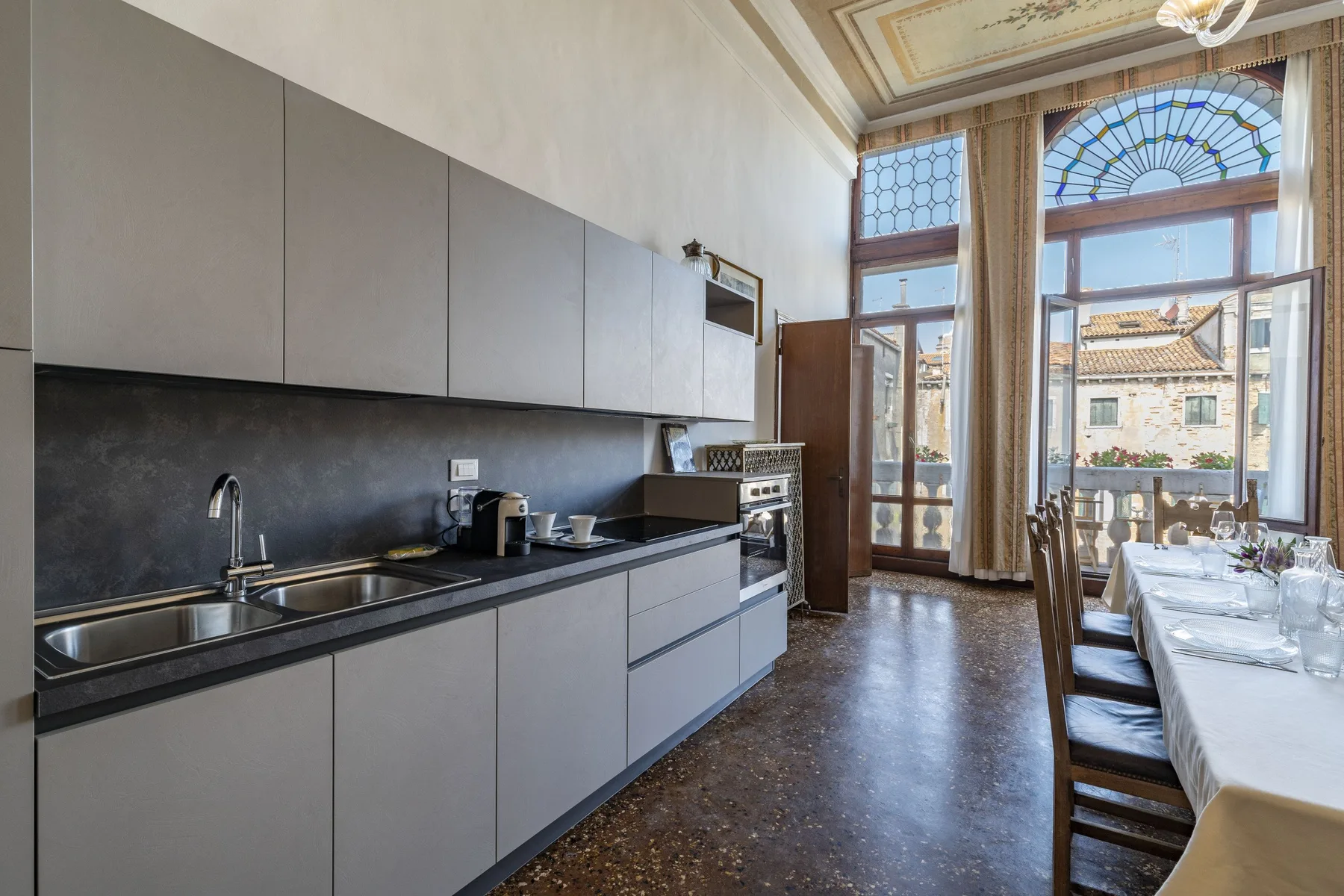 A kitchen and dining area with a long counter and a table beside tall windows.