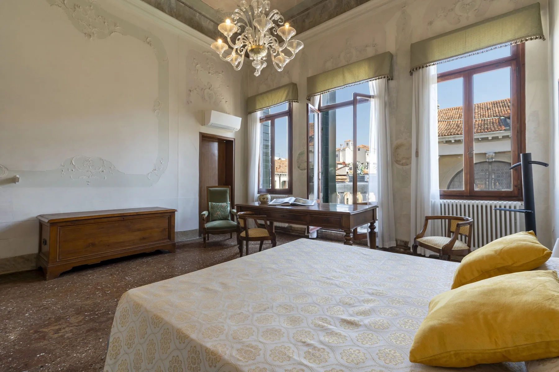 A bedroom with a large bed, wooden furnishings, and tall windows.