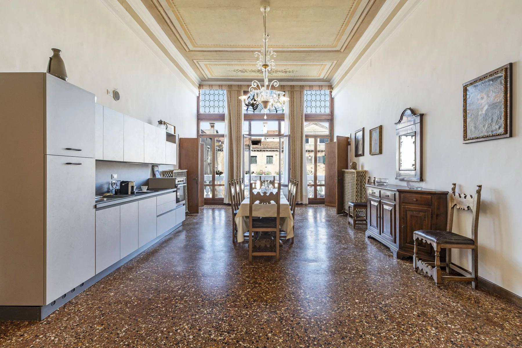 A long dining room with a table beneath a chandelier and cabinets along one wall.