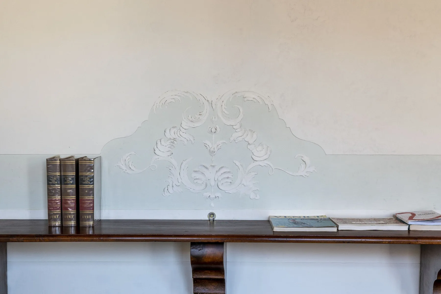 A decorative wall relief above a long wooden shelf with books.