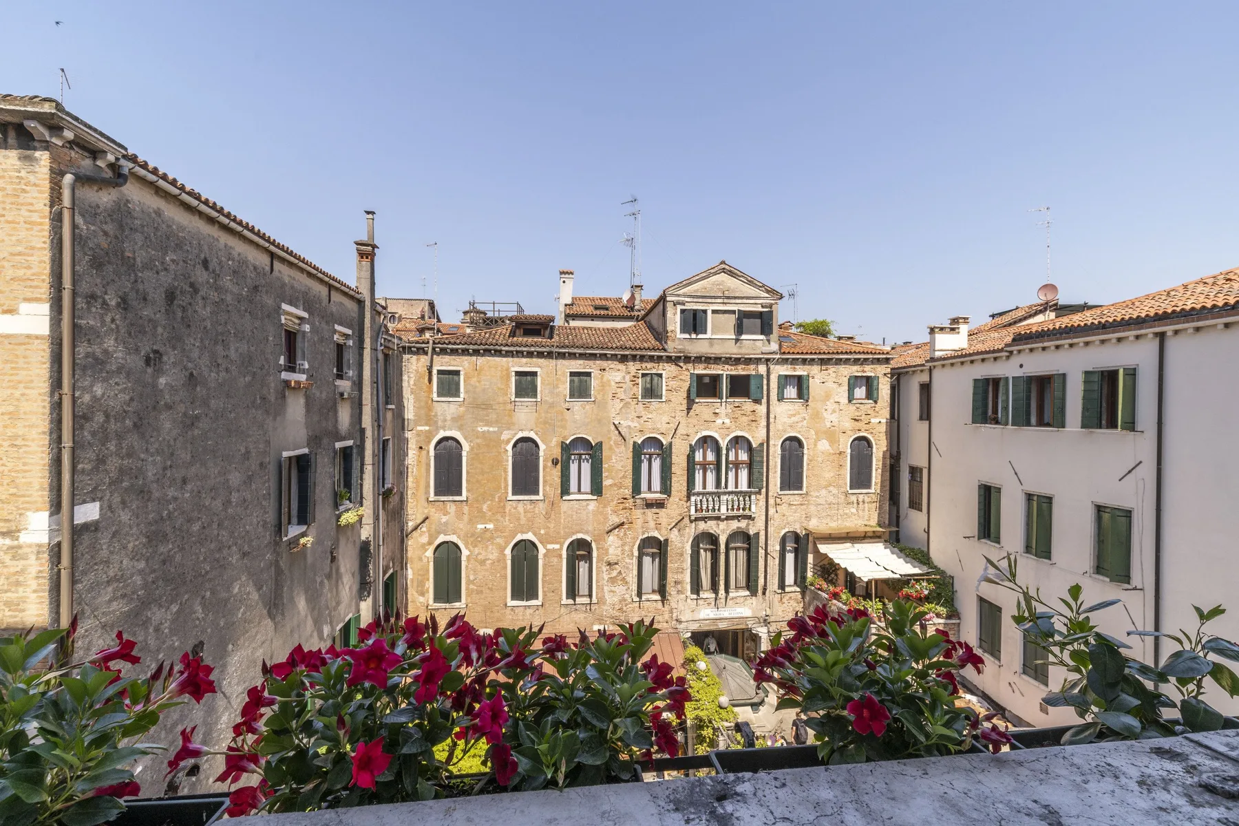A courtyard framed by historic buildings, with flowering plants along the foreground.