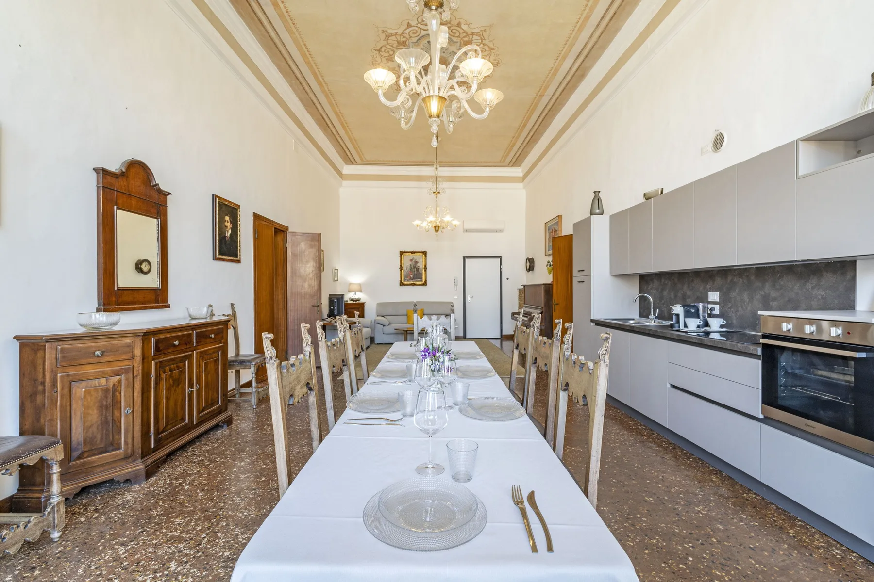 A long dining table with place settings sits beside a kitchen.