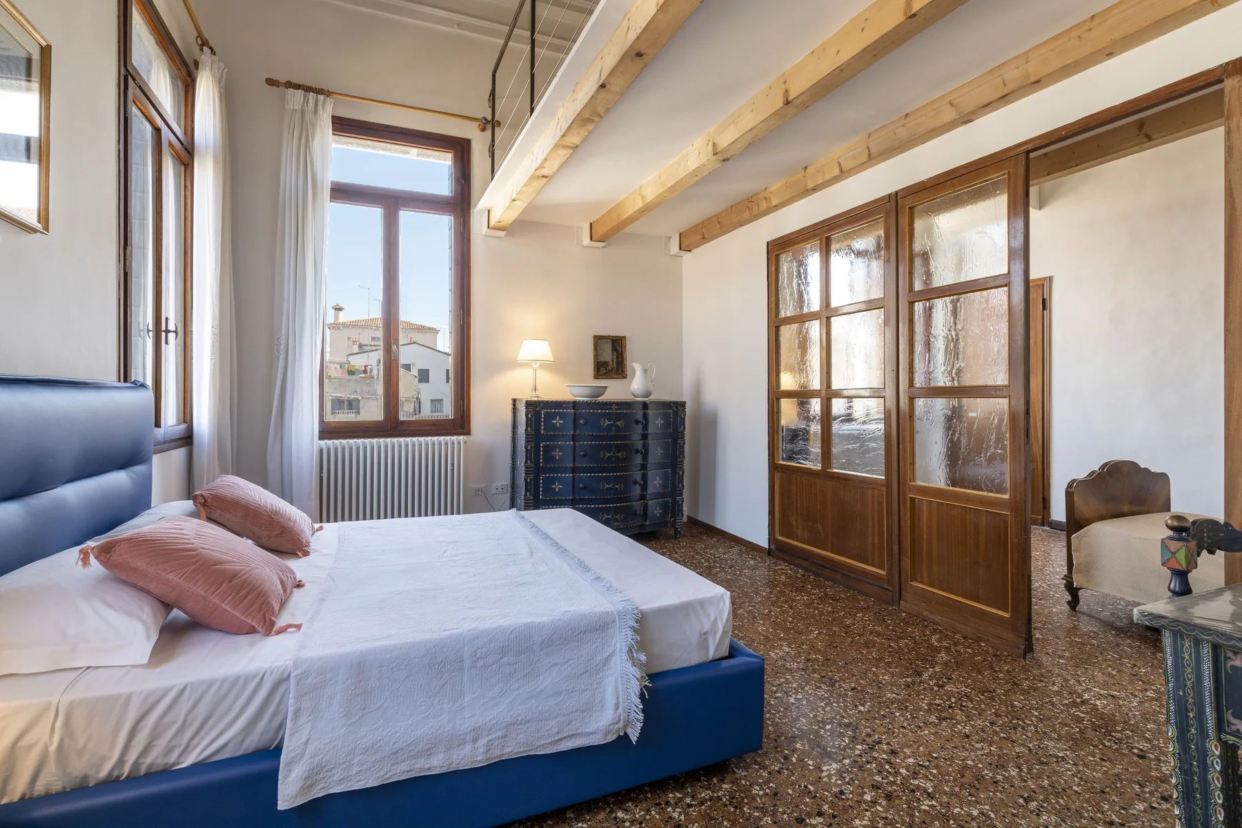 Bedroom with a bed, wooden-framed glass doors, and exposed ceiling beams.