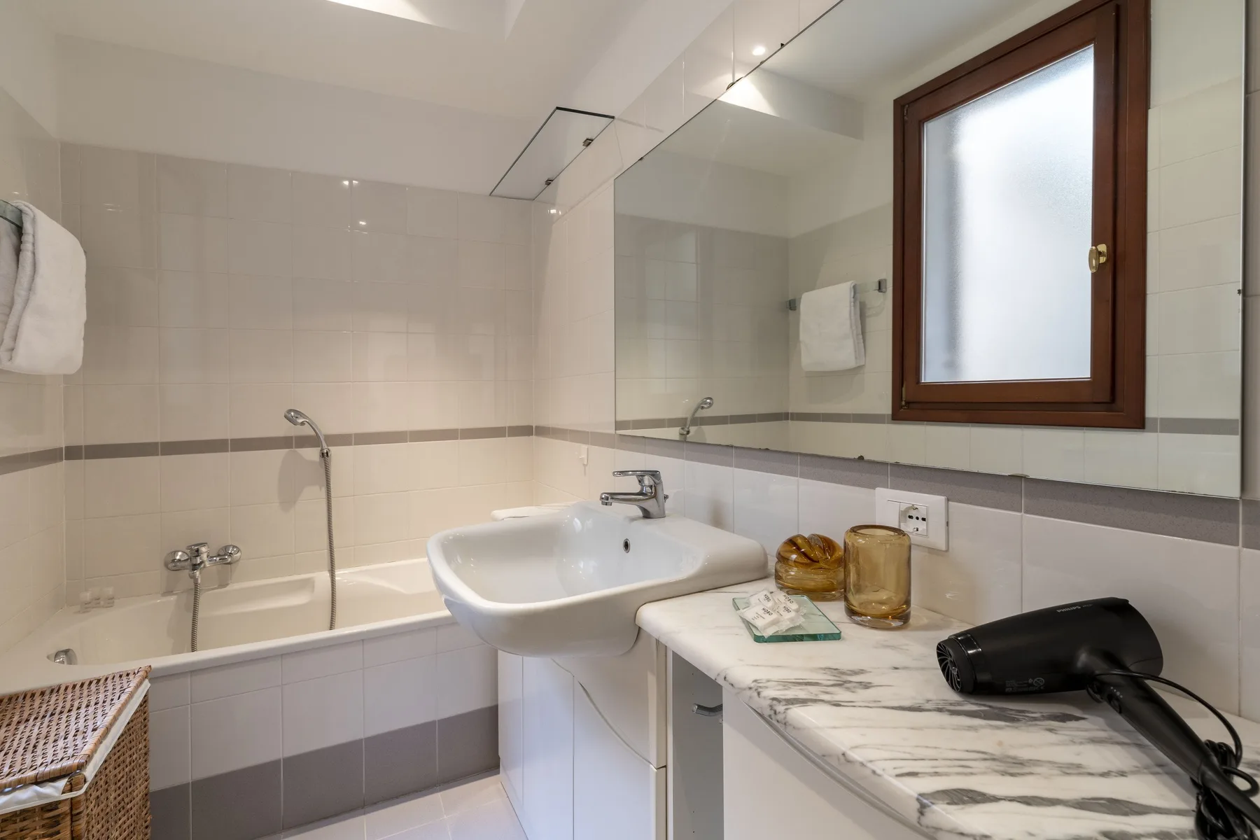 A tiled bathroom with a bathtub, sink, and countertop beneath a window.