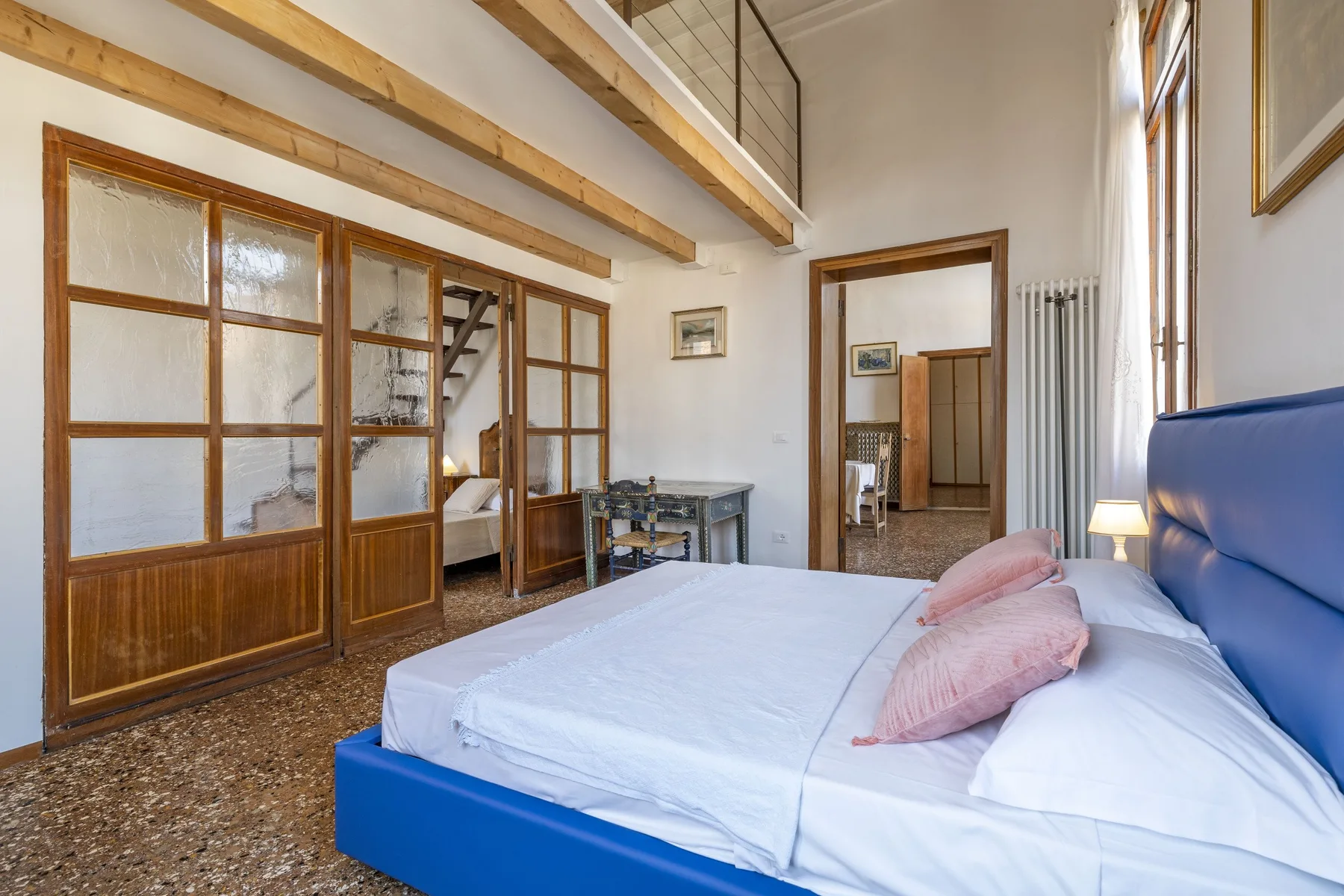 A bright bedroom with a blue bed beside wood-framed glass partitions.