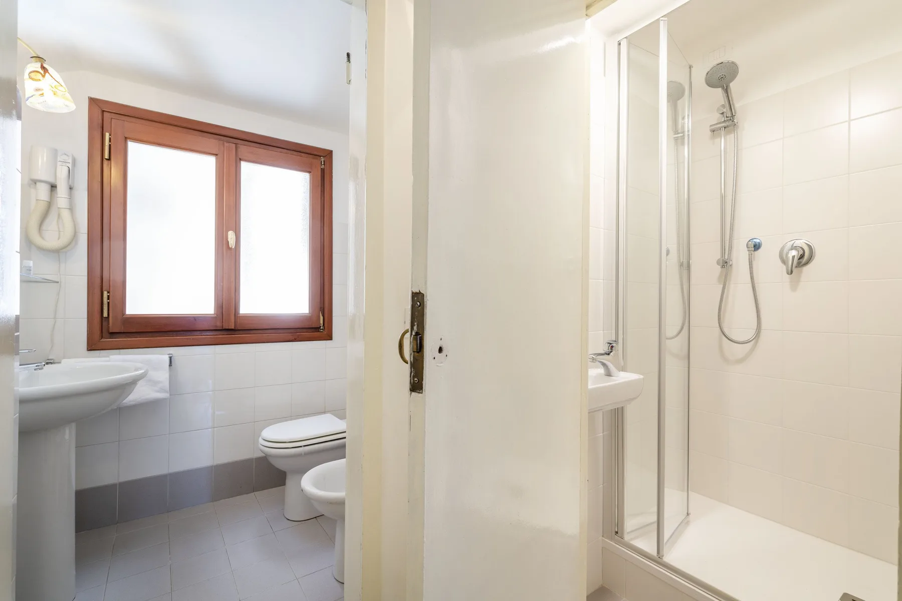 A bathroom with a shower, sink, and toilet beside a window.