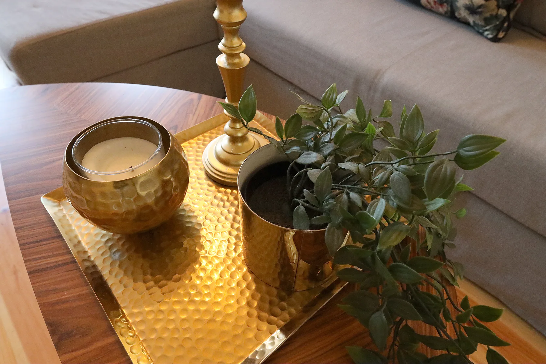 A living room coffee table holds a decorative tray, candle, lamp, and leafy plant.