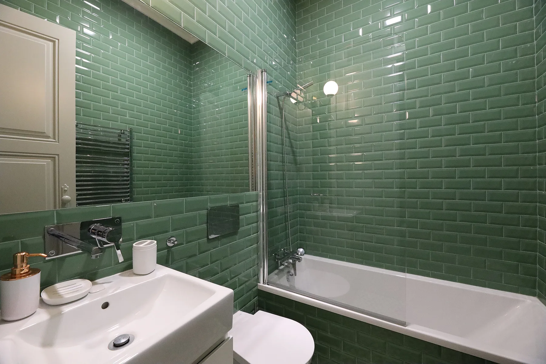 A bathroom with a white sink and bathtub against green tiled walls.