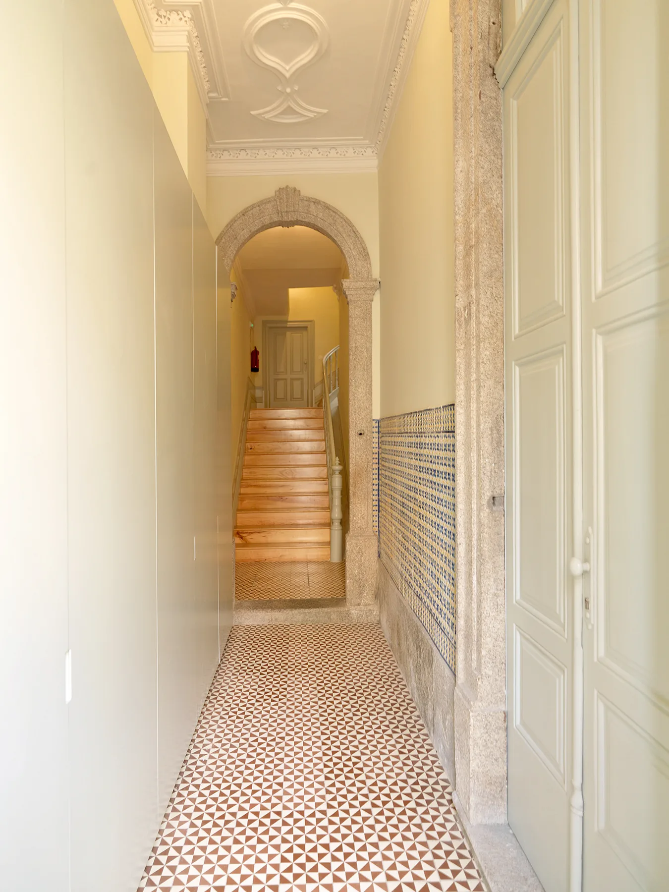 A narrow tiled hallway leads through an arched opening to a staircase.