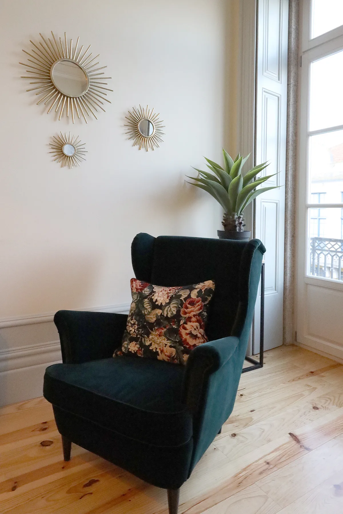 A dark upholstered armchair sits beside a tall window in a bright room.