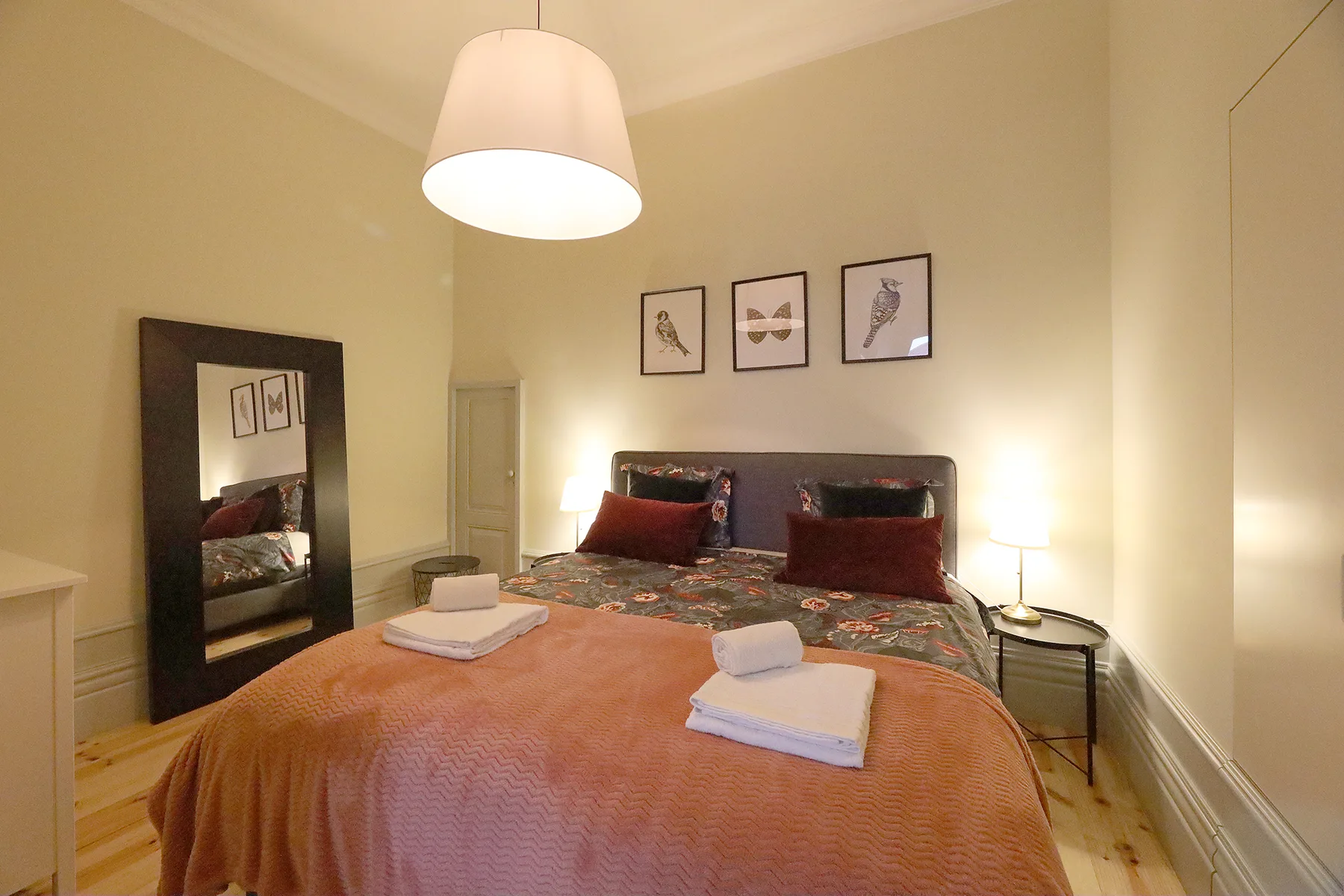 A bedroom with a bed, folded towels, and framed artwork above the headboard.