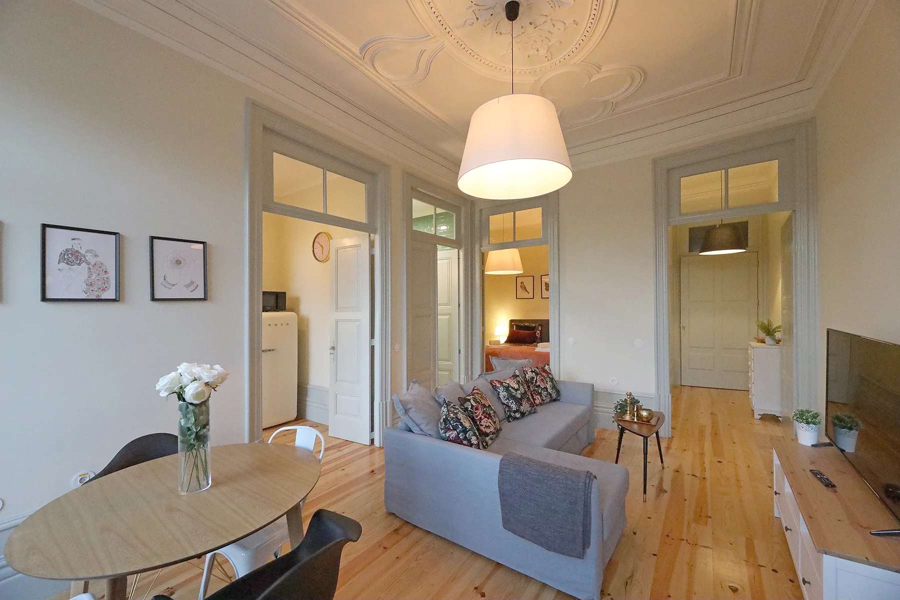 A bright living room has a sofa, dining table, and wooden floors.