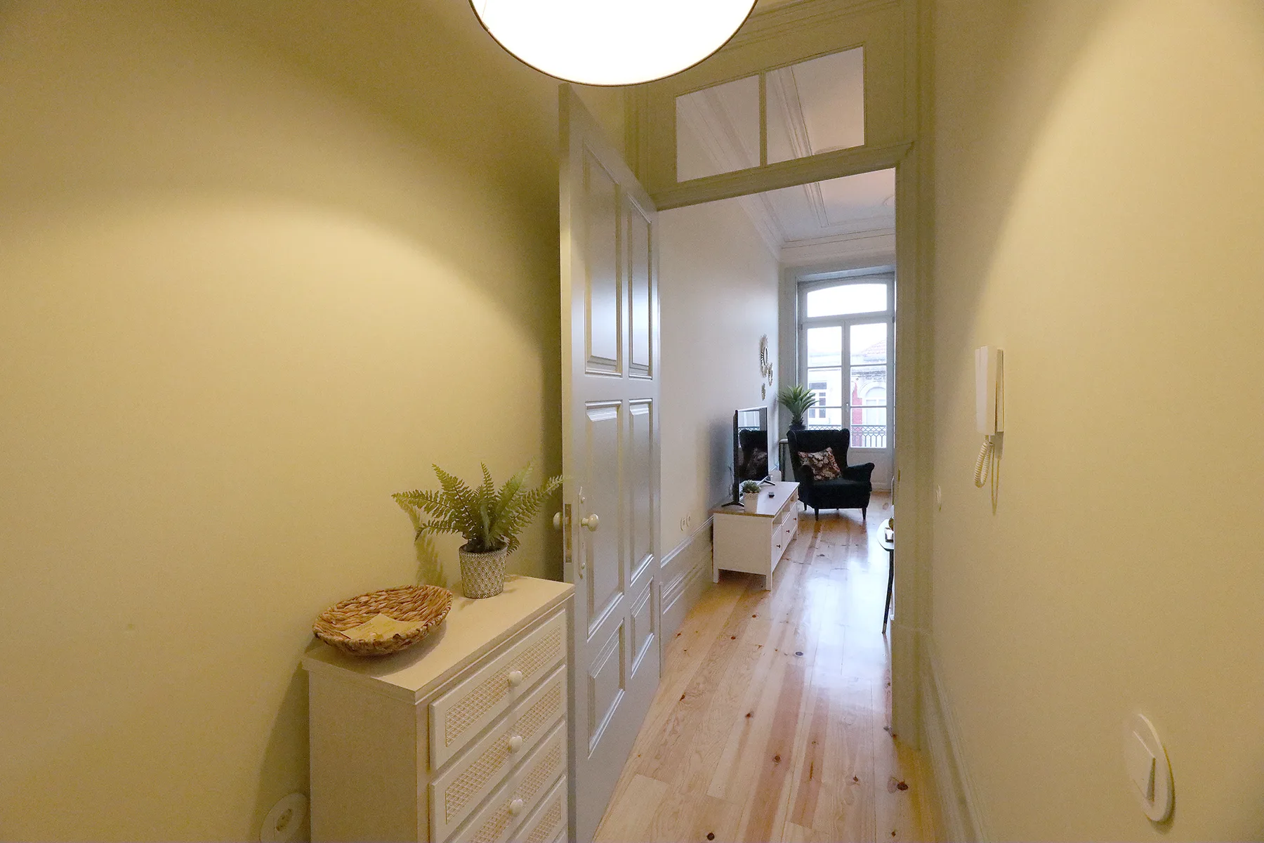 A bright hallway with a light wood floor leads toward a sitting area.