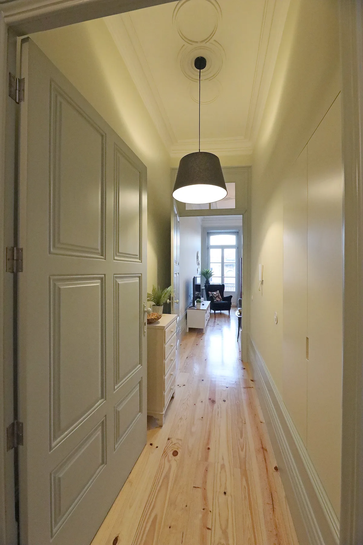 A narrow hallway with a wooden floor leads toward a bright sitting area.