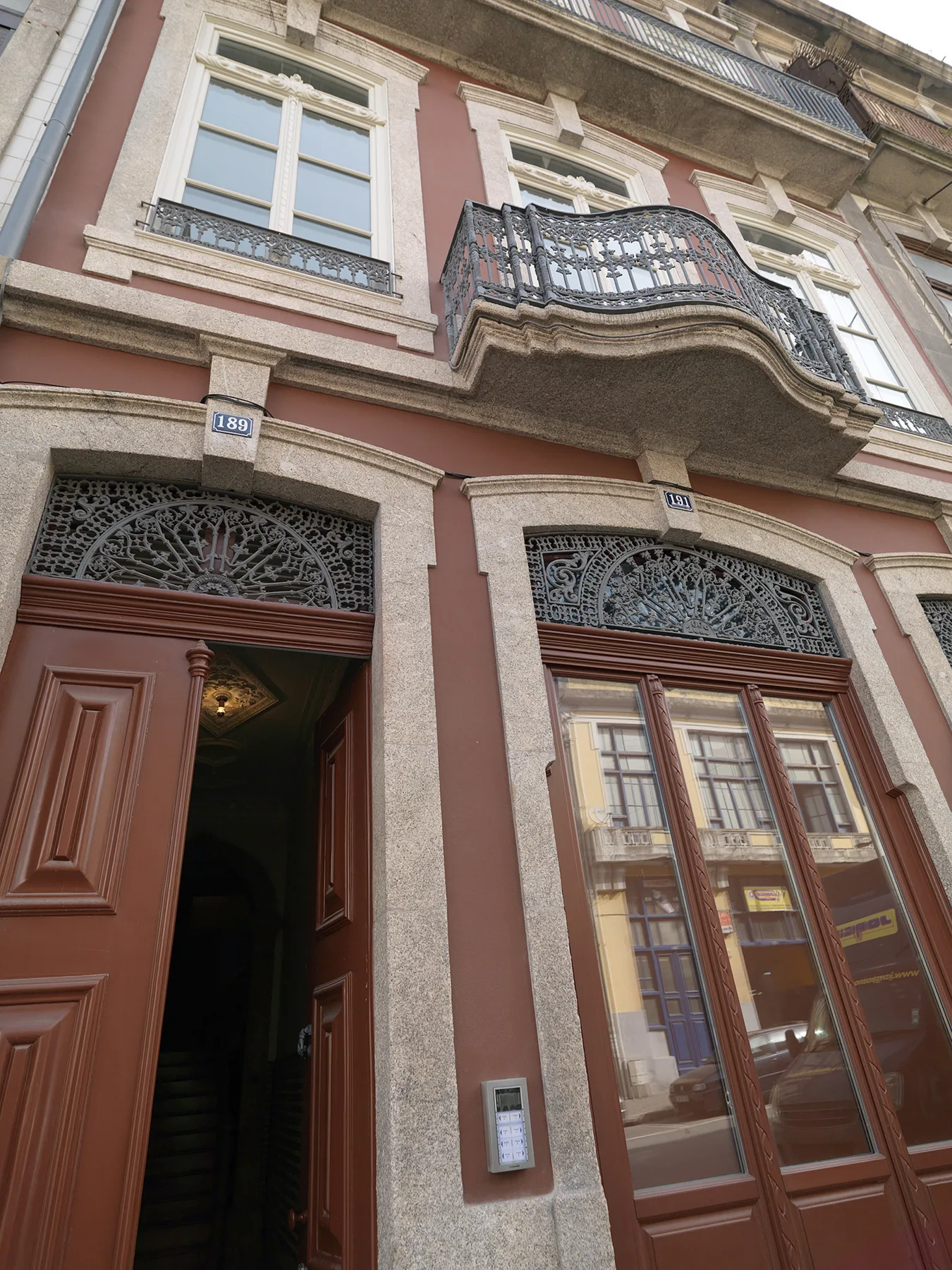 A pink building facade with ornate windows, a balcony, and an open doorway.