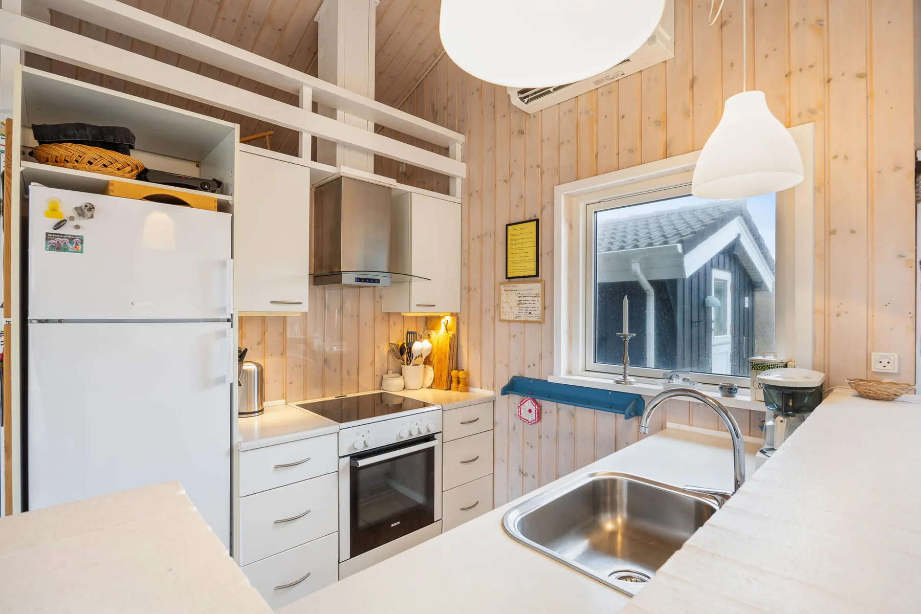 Una cocina compacta con armarios blancos, una estufa y un fregadero bajo la ventana.
