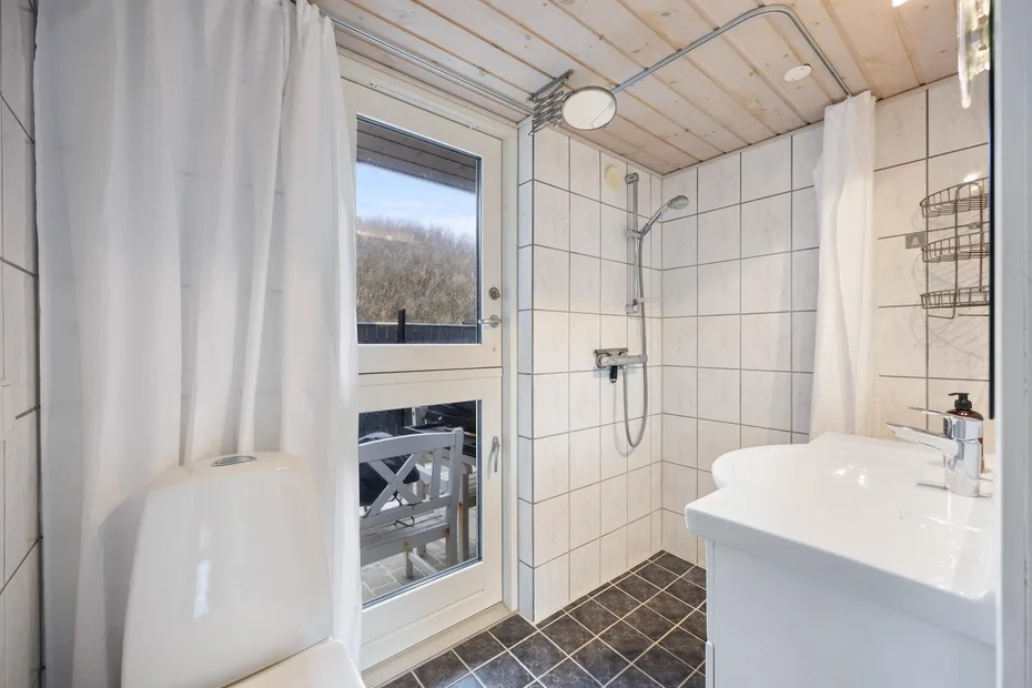 Un baño alicatado con ducha, lavabo y una puerta de cristal con vistas al exterior.