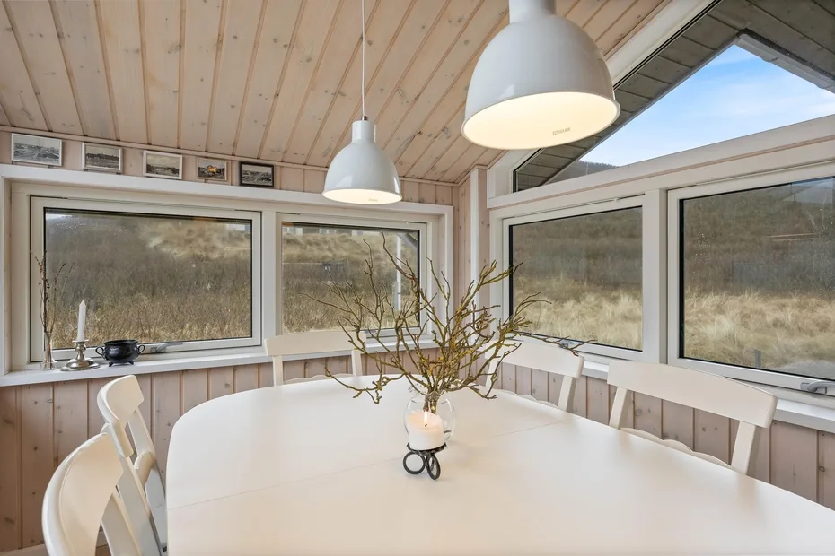 Un comedor con una mesa blanca y grandes ventanas.
