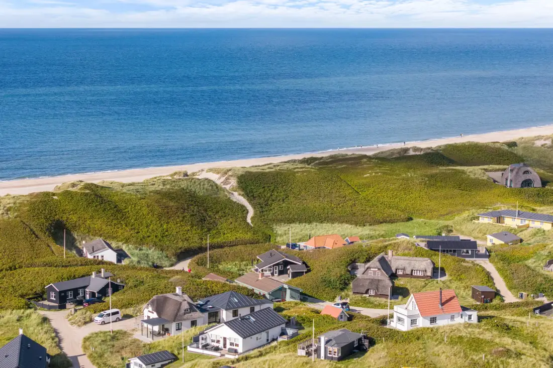 Una vista aérea muestra casas costeras entre dunas verdes junto al mar.