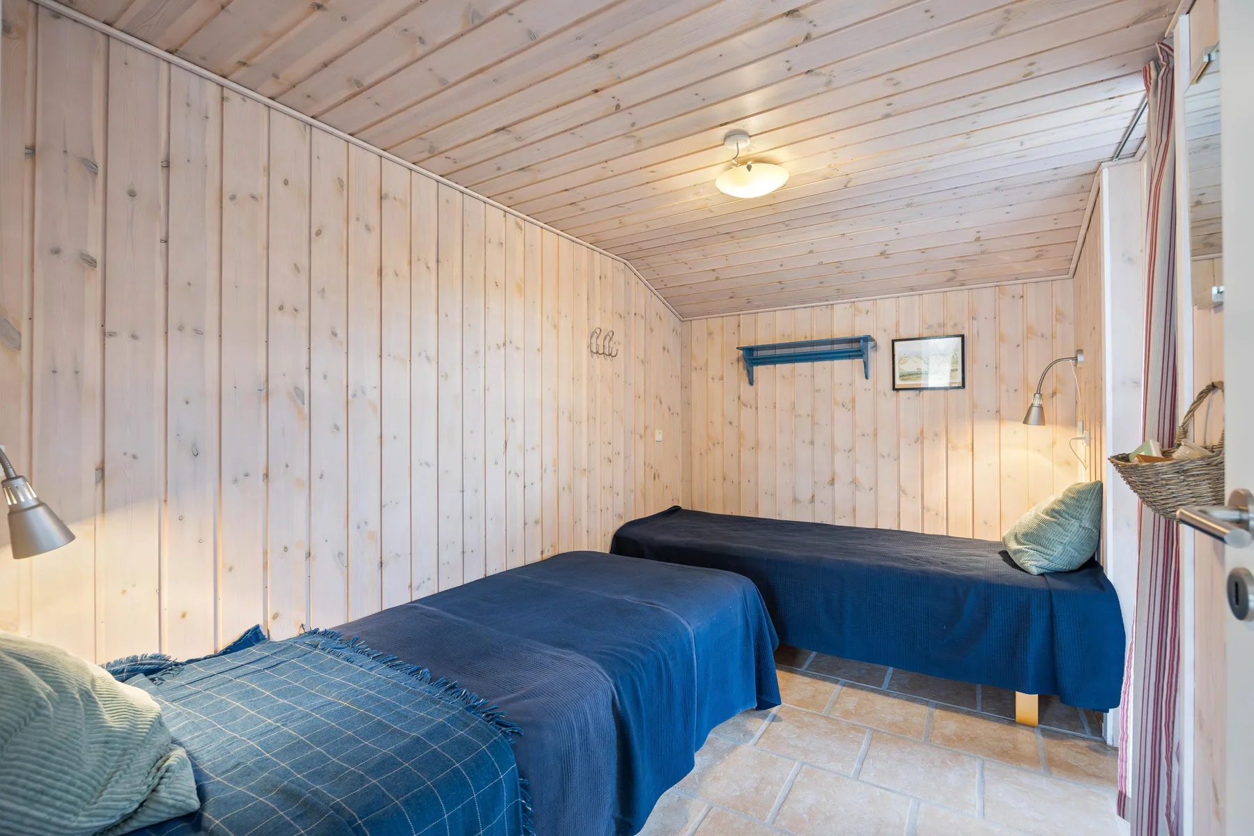 Dormitorio revestido de madera con dos camas cubiertas con ropa de cama azul.