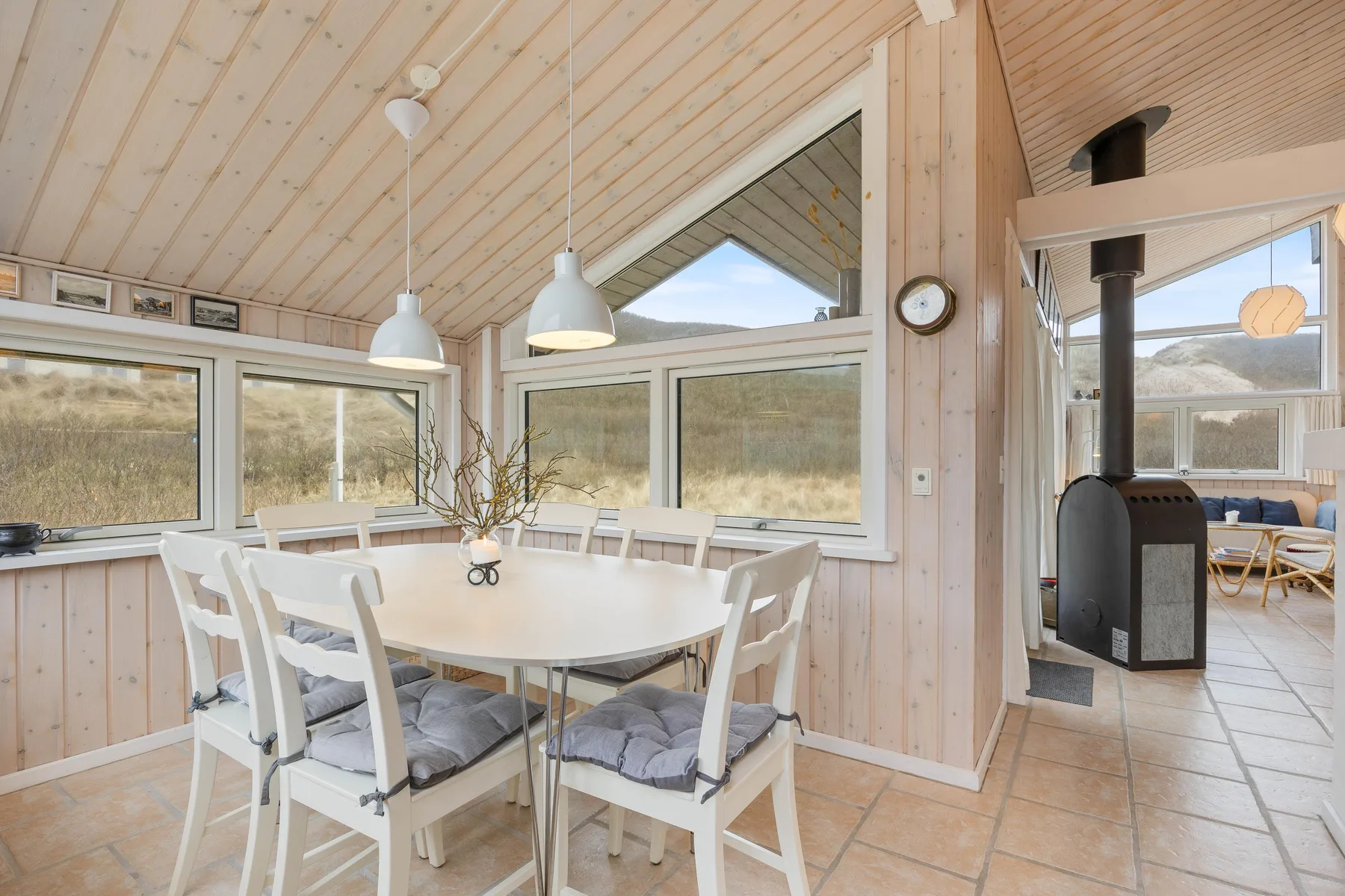 Un comedor luminoso con una mesa junto a grandes ventanas y una estufa de leña.