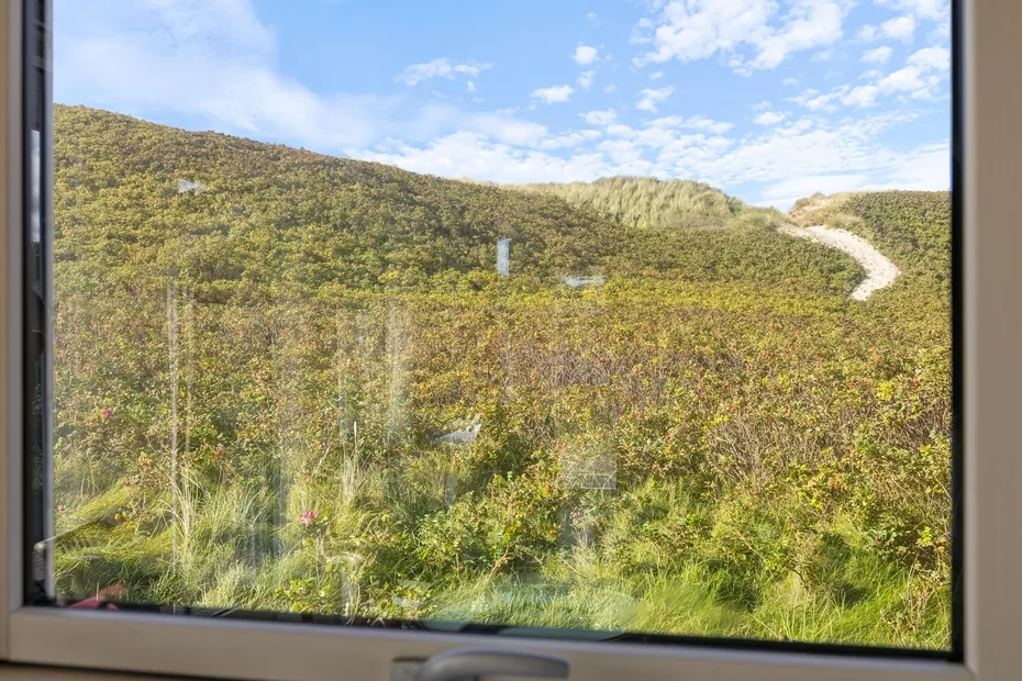 Una vista a través de una ventana muestra colinas verdes bajo un cielo parcialmente nublado.