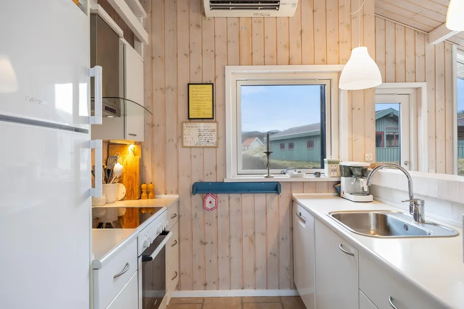 Una cocina compacta con paredes revestidas de madera clara y un fregadero de acero inoxidable.