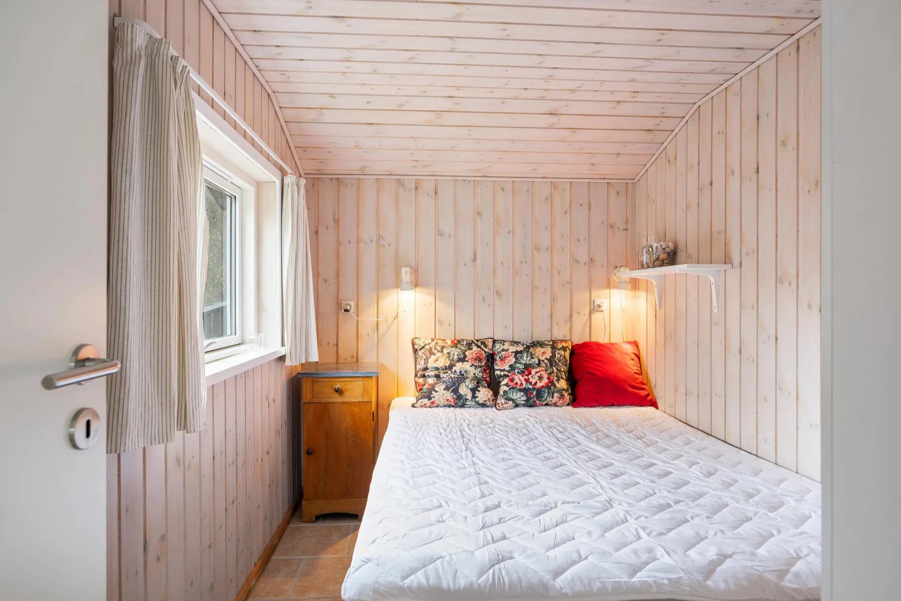 Un dormitorio pequeño con una cama, cojines estampados y una ventana.