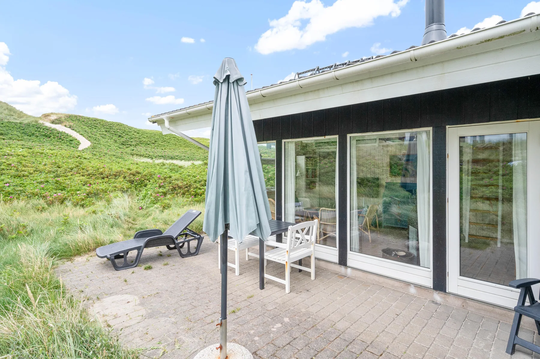 Un patio con asientos al aire libre y una sombrilla junto a una casa con fachada acristalada.