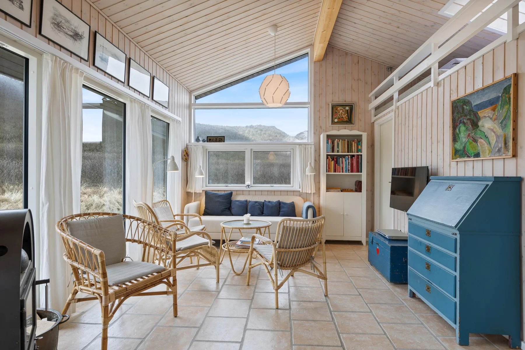 Una sala de estar luminosa con asientos de mimbre y grandes ventanas con vistas al paisaje.