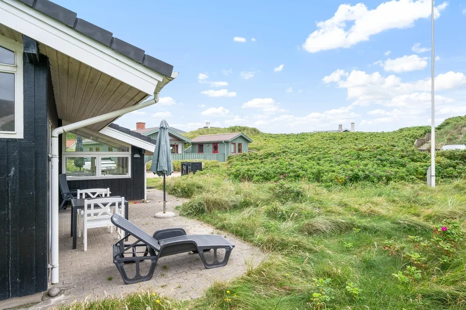 Un patio con asientos al aire libre da a dunas cubiertas de hierba y una casa cercana.