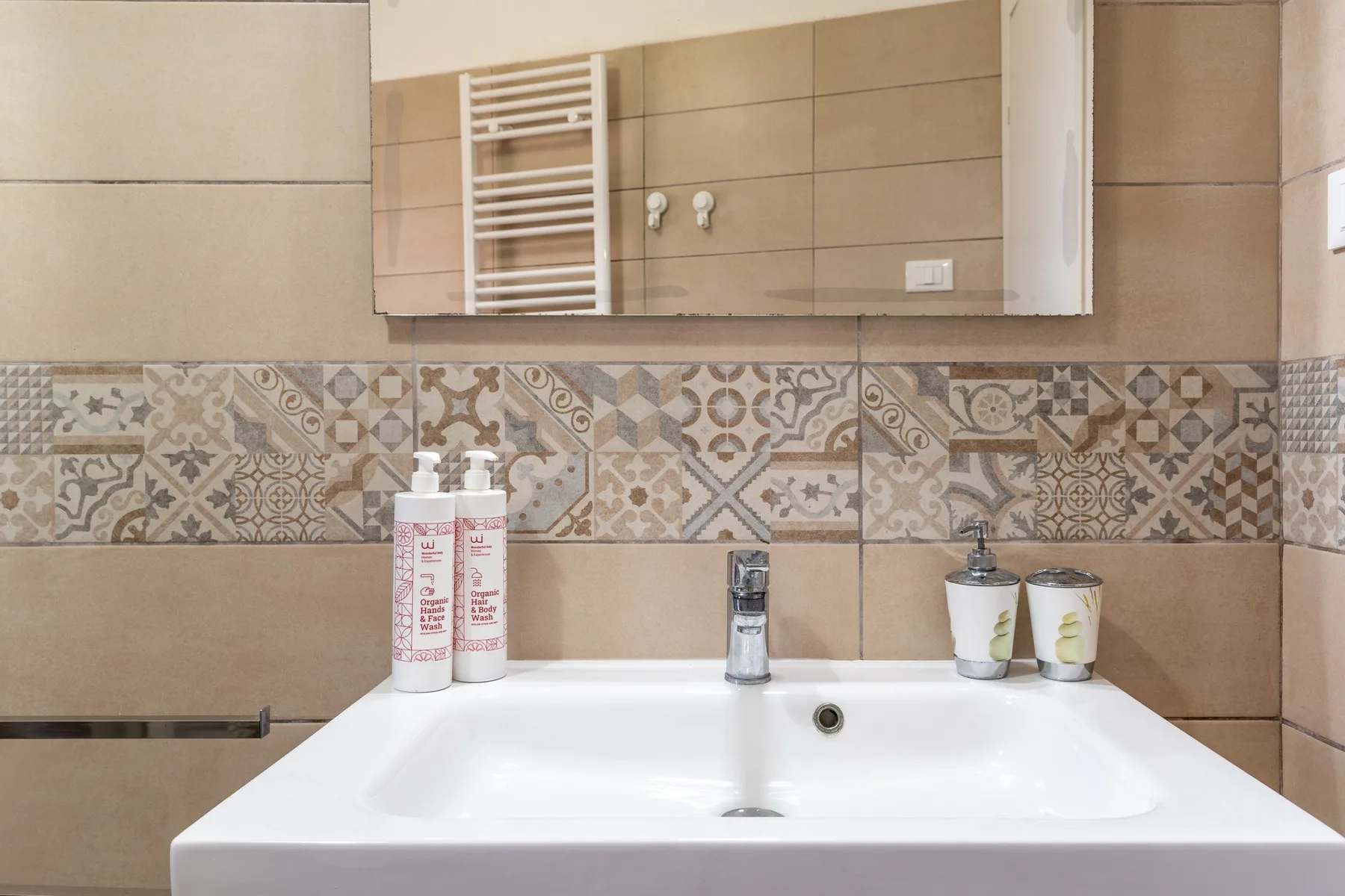 Un lavabo de baño está bajo un armario con espejo, con azulejos decorados en la pared.