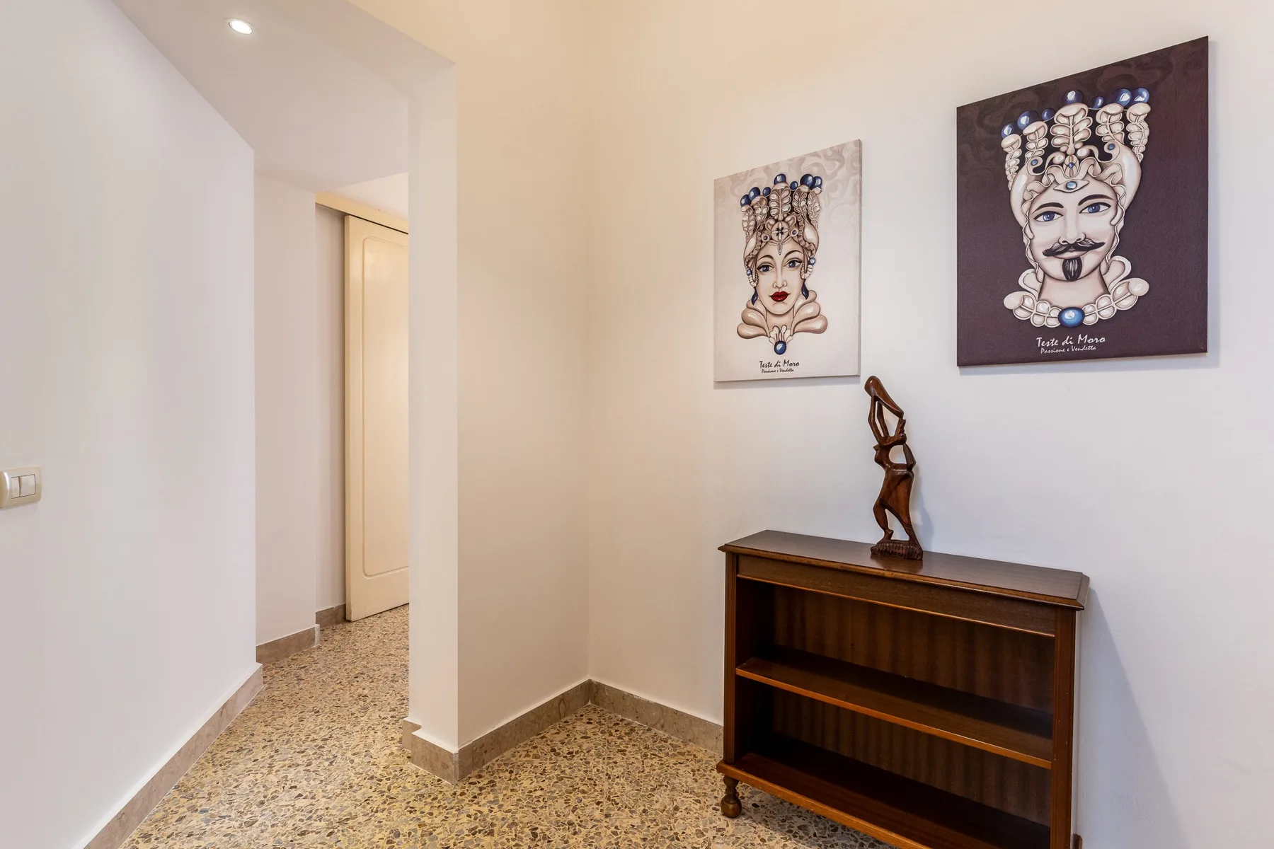 Una entrada con un mueble de estantes de madera y dos retratos en la pared.